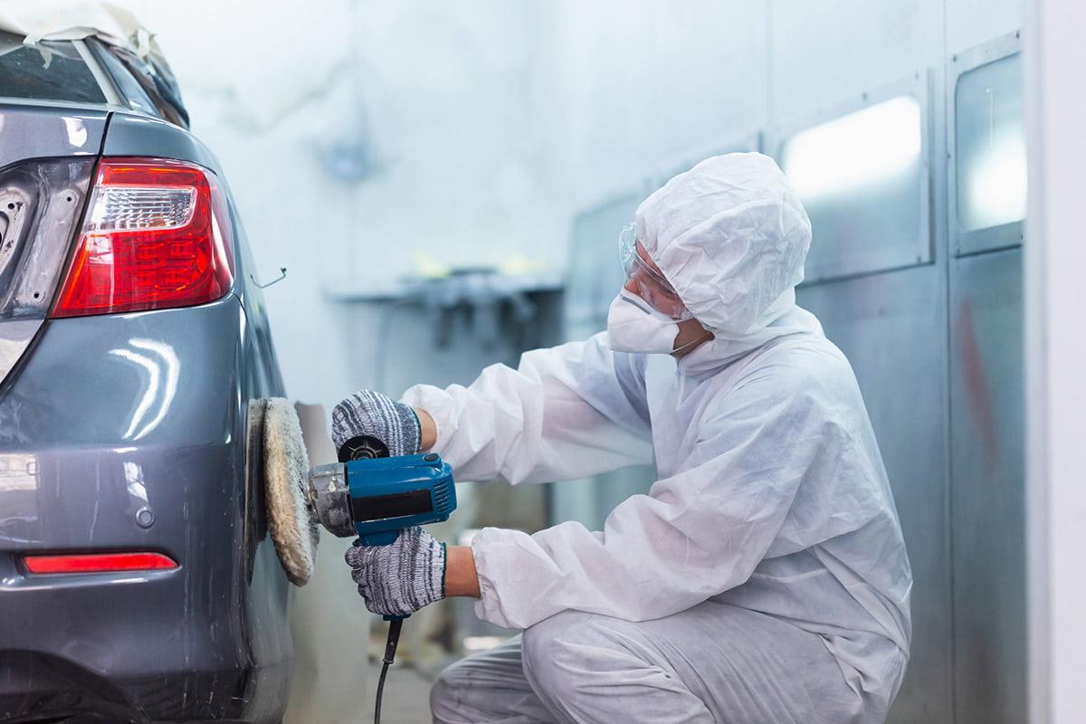 San Juan College student standing in front of a car frame in the auto body shop